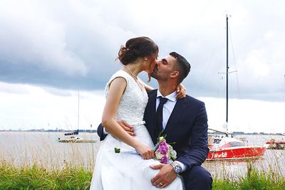 Young couple holding hands while standing by sea against sky