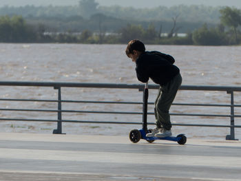 Side view of boy with push scooter by railing