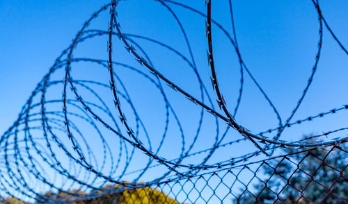 Low angle view of barbed wire fence against blue sky