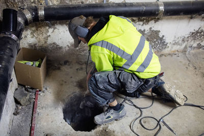 High angle view of plumber drilling floor in basement