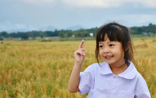 Portrait of cute girl standing on field against sky