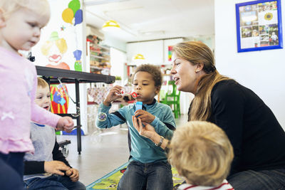 Happy teacher and children playing with bubbles in kindergarten