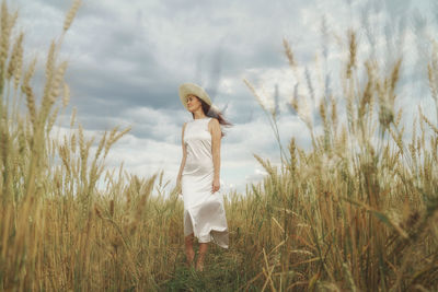 Woman standing on weat field against sky