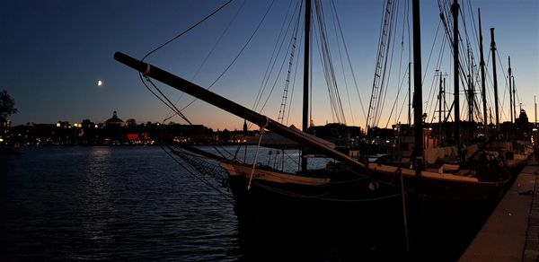 Sailboats moored in harbor at sunset