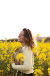 Beautiful young woman standing by yellow flower on field against sky