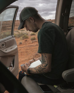 Side view of man with book and pen sitting in car