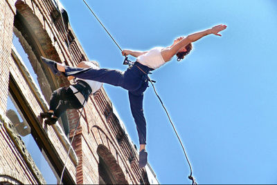 Low angle view of people hanging on rope against clear blue sky