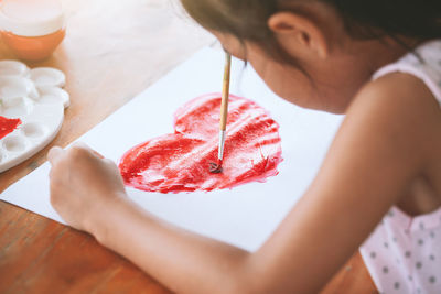 Close-up of girl painting heart shape on paper in porch