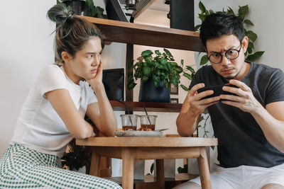 Side view of young friends using mobile phone while sitting at table
