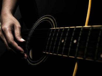 Midsection of man playing guitar against black background