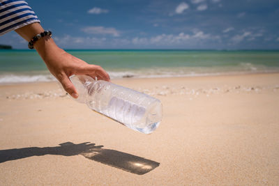 Close-up of hand holding bottle by sea against sky