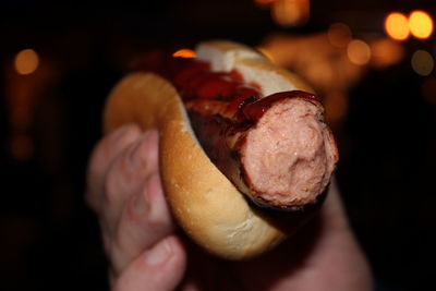 Cropped hand holding hot dog at night