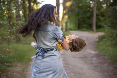 Young woman plays with toddler girl in yellow in park