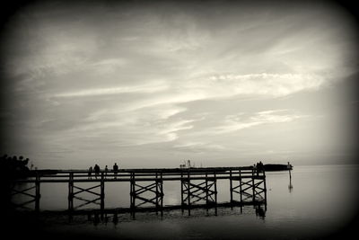 Silhouette built structure by sea against cloudy sky