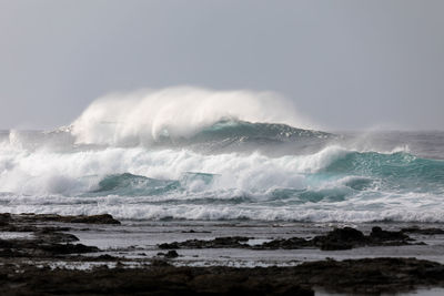 Scenic view of sea waves crashing on shore against clear sky