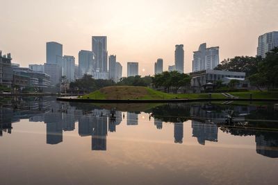 Reflection of modern buildings in river against sky in city