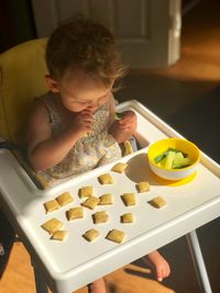 High angle view of cute baby girl eating food while sitting on high chair at home