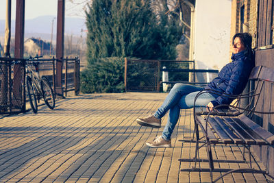 Full length of woman sitting on bench at railroad station platform