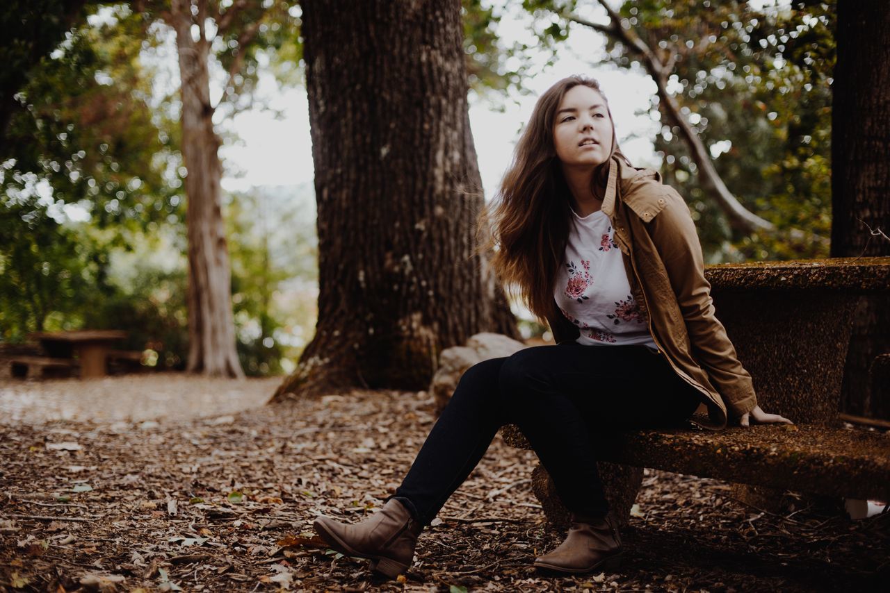 tree, one person, casual clothing, real people, tree trunk, front view, leisure activity, young women, full length, young adult, day, nature, lifestyles, outdoors, smiling, beautiful woman, people