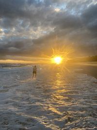 Man standing in sea against sky during sunset