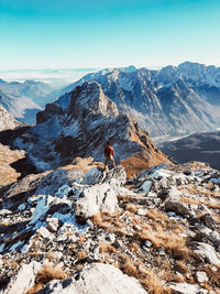 Midsection of person on rock by snowcapped mountain against sky