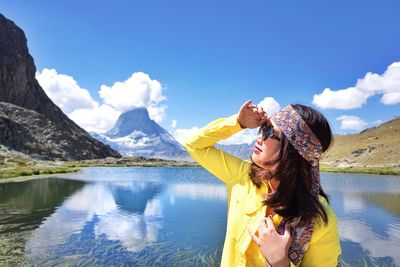 Woman shielding eyes while standing against lake and mountains
