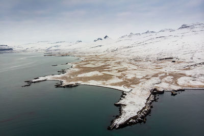 Aerial view of snowcapped mountains by sea against sky