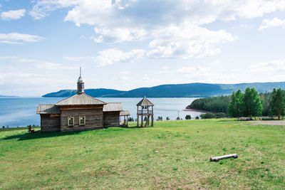 An old wooden russian house with a bell tower on the river bank on a summer day