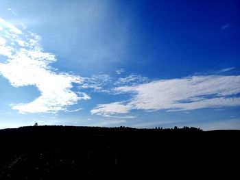 Low angle view of silhouette landscape against blue sky
