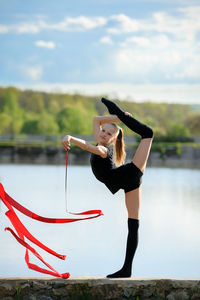 Side view of girl with ribbon standing on retaining wall against lake