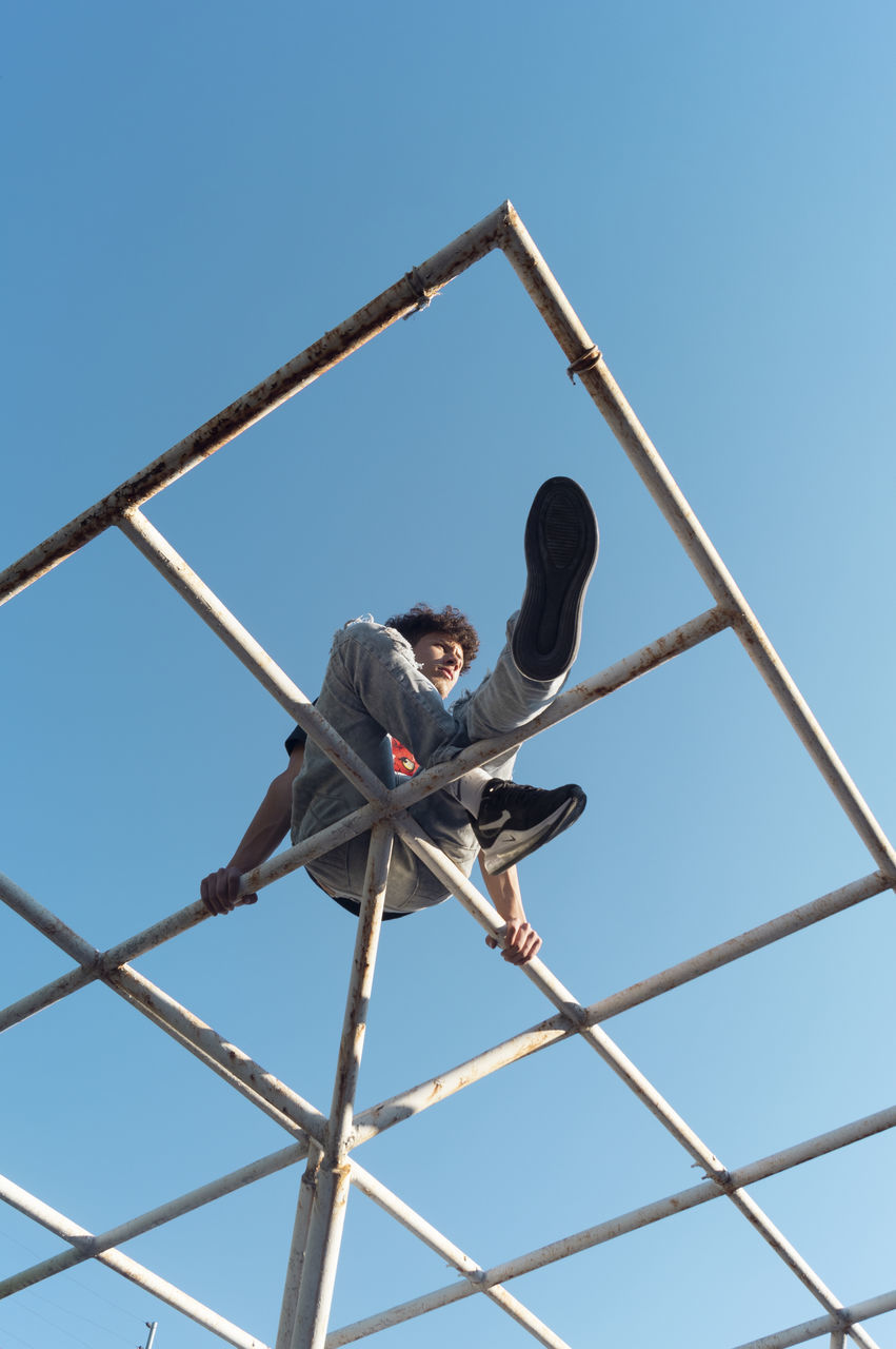 low angle view, sky, clear sky, men, real people, nature, blue, full length, day, people, metal, balance, occupation, architecture, working, casual clothing, built structure, sunlight, outdoors