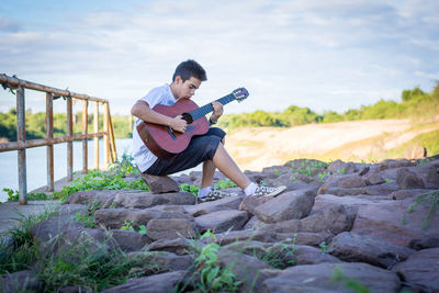 Young woman playing guitar on rock
