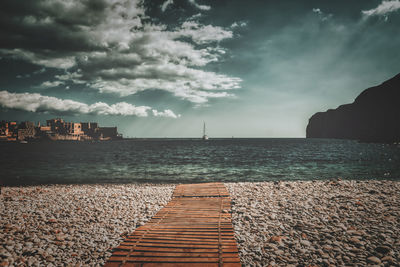 Scenic view of footbridge on a stony beach at sea against sky