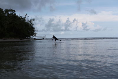 Silhouette fisherman throwing fishing net in sea against cloudy sky