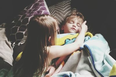 High angle view of girl touching sleeping brother on bed at home