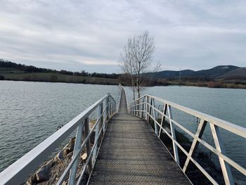 Wooden footbridge over lake against sky