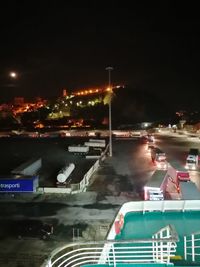 Illuminated city by road against sky at night