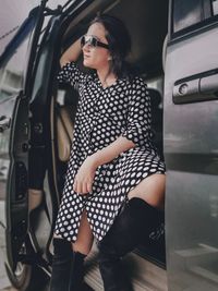 A girl wearing a polkadot dress, sun glasses and high boots sitting in a car 