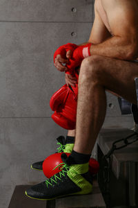 Low section of shirtless man holding gloves while sitting on steps