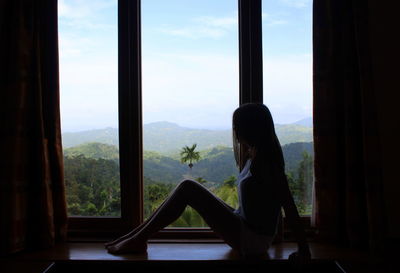 Side view of woman sitting at window