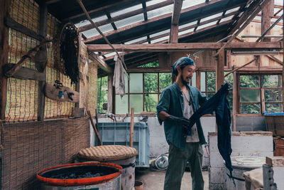 Man holding clothing while standing in shed