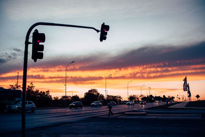 Silhouette traffic signal on road against cloudy sky during sunset