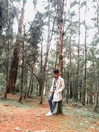 Full length of man standing by tree trunk in forest