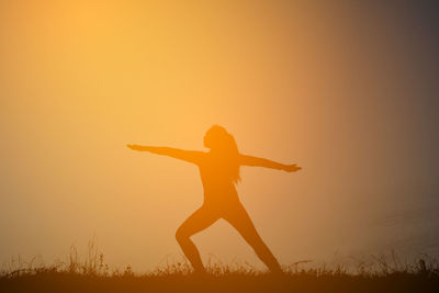 Silhouette woman exercising warrior 2 on field