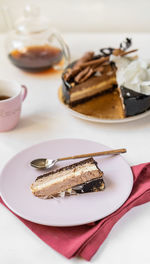 Delicious three chocolates cake slice on plate with tea on white background