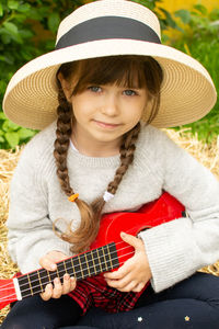 Portrait of smiling girl wearing hat playing guitar