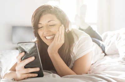 Young woman using mobile phone while sitting on bed