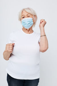 Senior woman wearing mask gesturing against white background