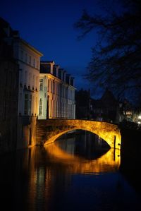 Arch bridge over canal amidst buildings in city at night