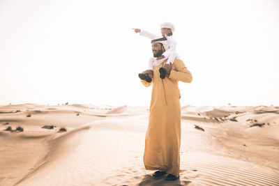 Full length of father carrying son on shoulder in desert